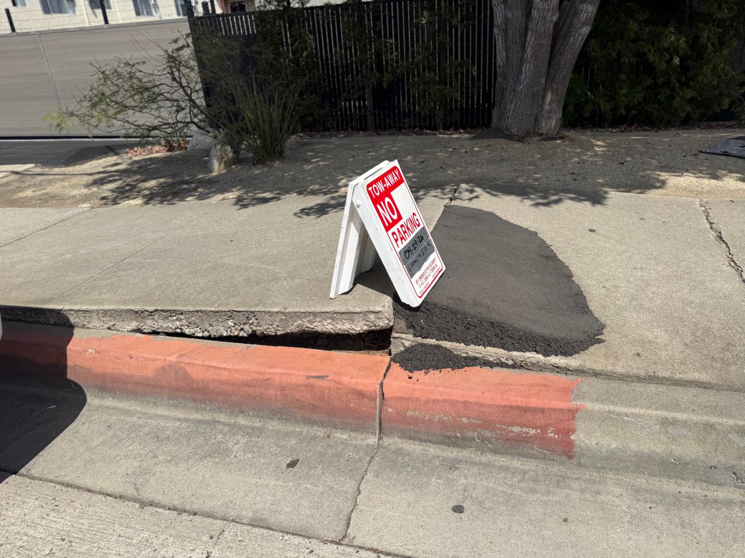 A lifted, cracked San Diego sidewalk with the City's temporary asphalt patch and a tow-away no-parking permit sign posted for the repair