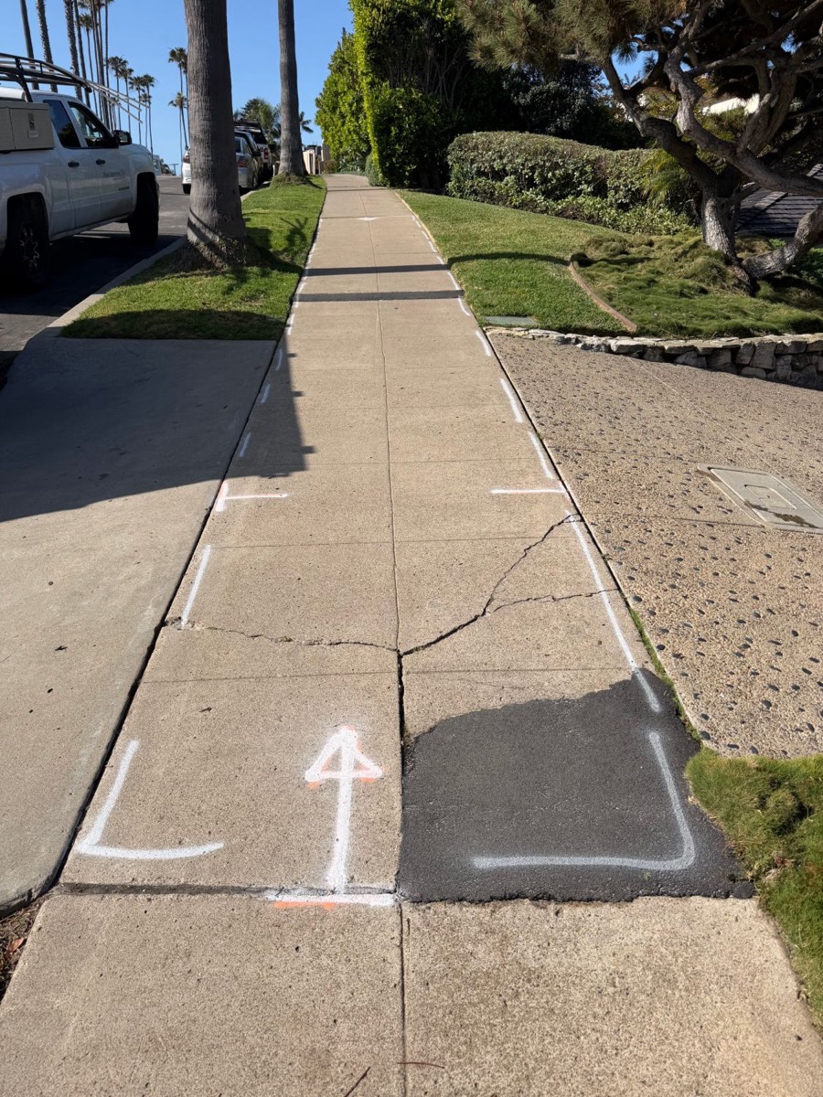 Cracked San Diego sidewalk with asphalt patch, marked by the City for replacement